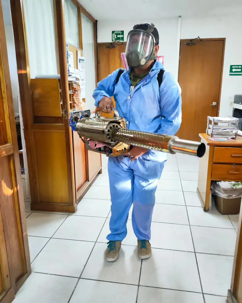 Técnico de Clean Control con traje azul y nebulizador caminando por un pasillo de oficinas